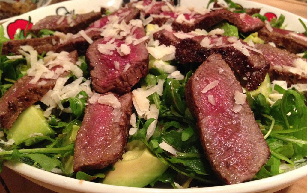 Un steak juteux sur un lit de roquette, accompagné d'un avocat onctueux et de parmesan